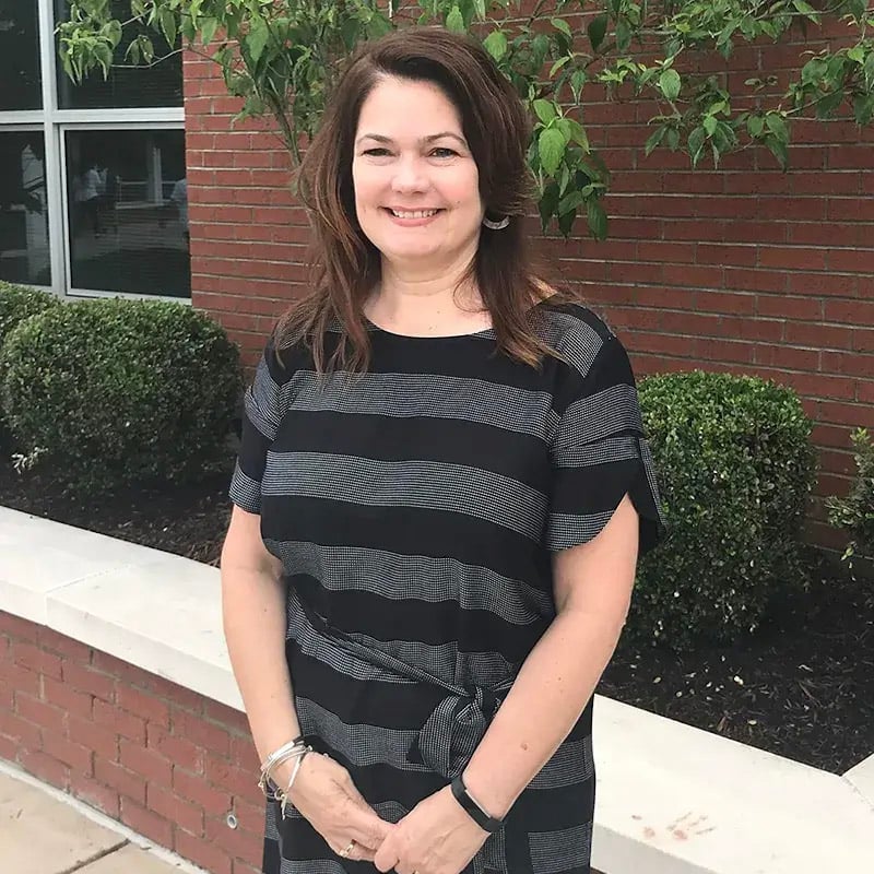 Mrs. Goode stands outside a brick building in a black and gray striped dress